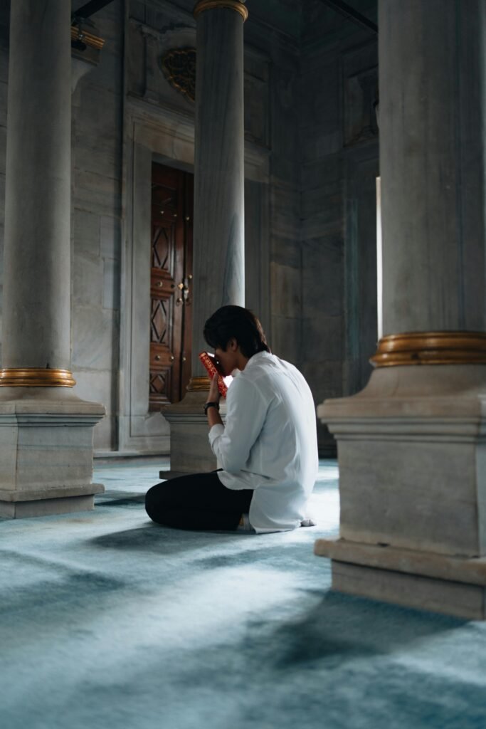 An individual kneels in prayer within a serene mosque, embodying spirituality and peace.